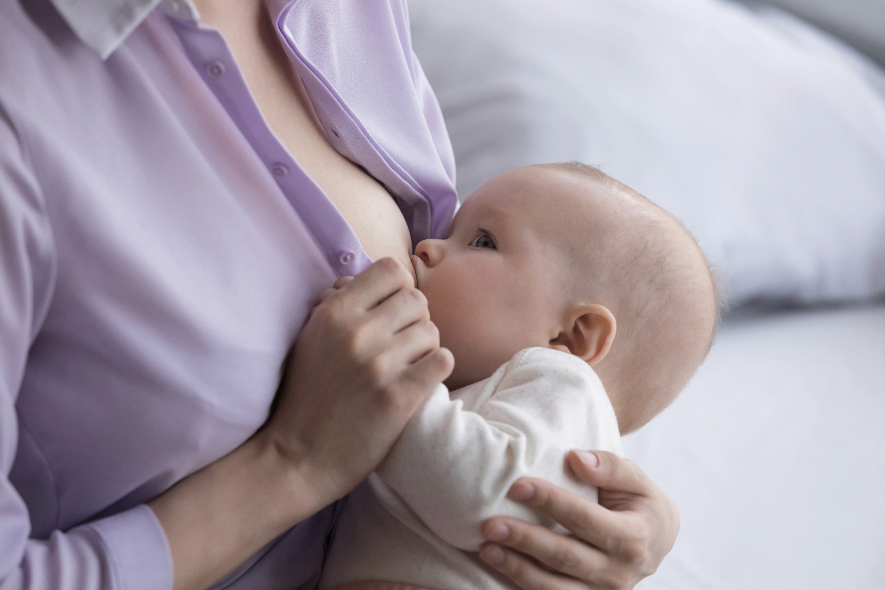 Rózsaszín ingben lévő édesanya szoptatja gyermekét.