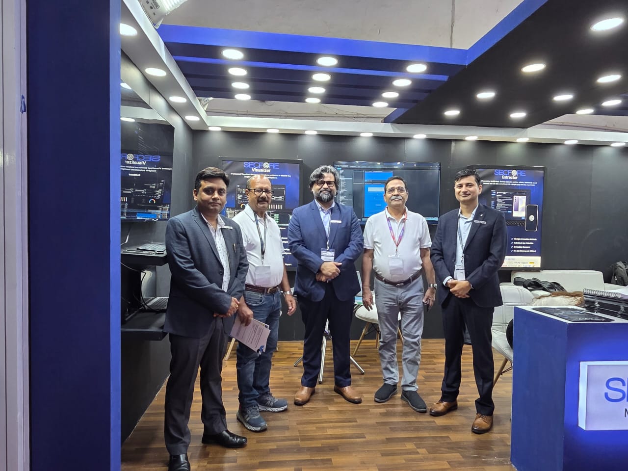 Five attendees posing at Secfore’s mobile forensics booth during the company’s official launch at International Police Expo 2025 in New Delhi, with product displays behind them.
