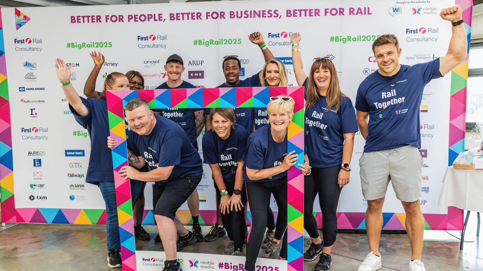 Outdoor team-building event with participants wearing matching blue shirts, taking part in inflatable obstacle courses and games, smiling and cheering, with the words 'ENTER A TEAM' in large bold white and green text across the image.