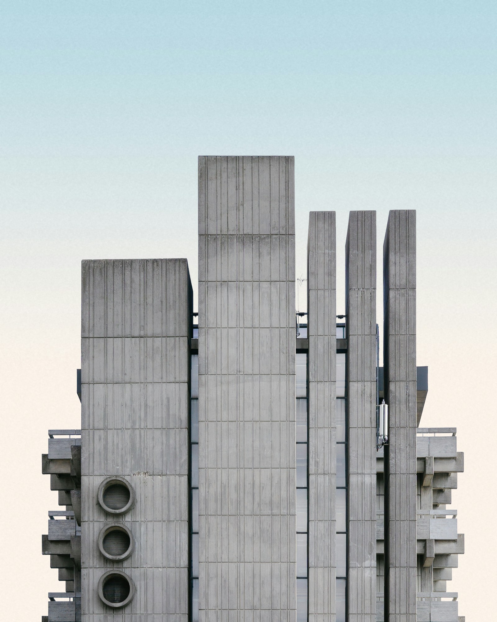 Brutalist concrete tower with round vents against a pale sky