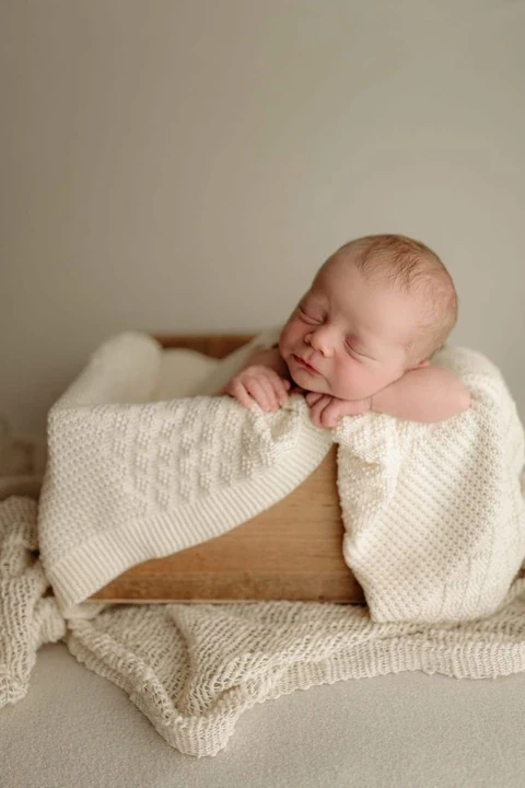 Sleeping newborn tucked in cream fabric inside a wooden box