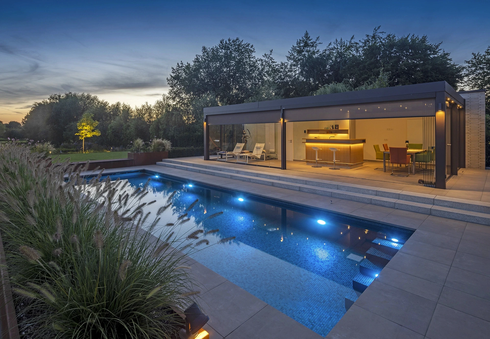 MLine Schwimmbad am Abend mit modernem Poolhaus, LED-Beleuchtung und Lichterketten