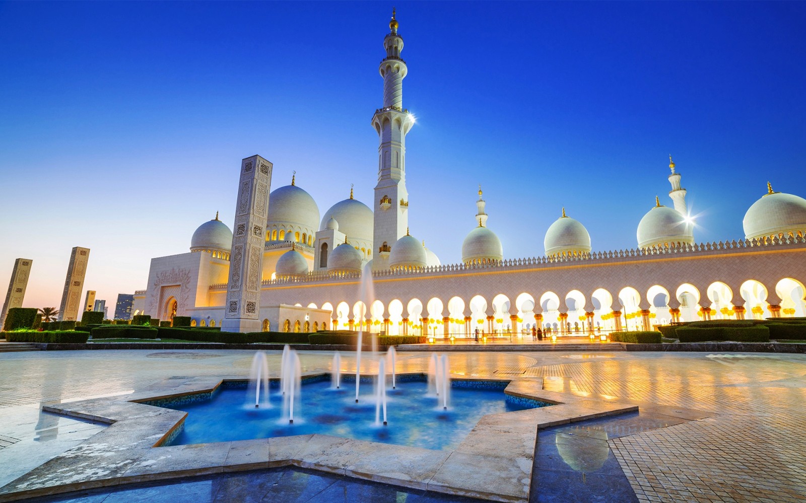 Sheikh Zayed Grand Mosque at dusk, Abu Dhabi, with illuminated arches and fountains.