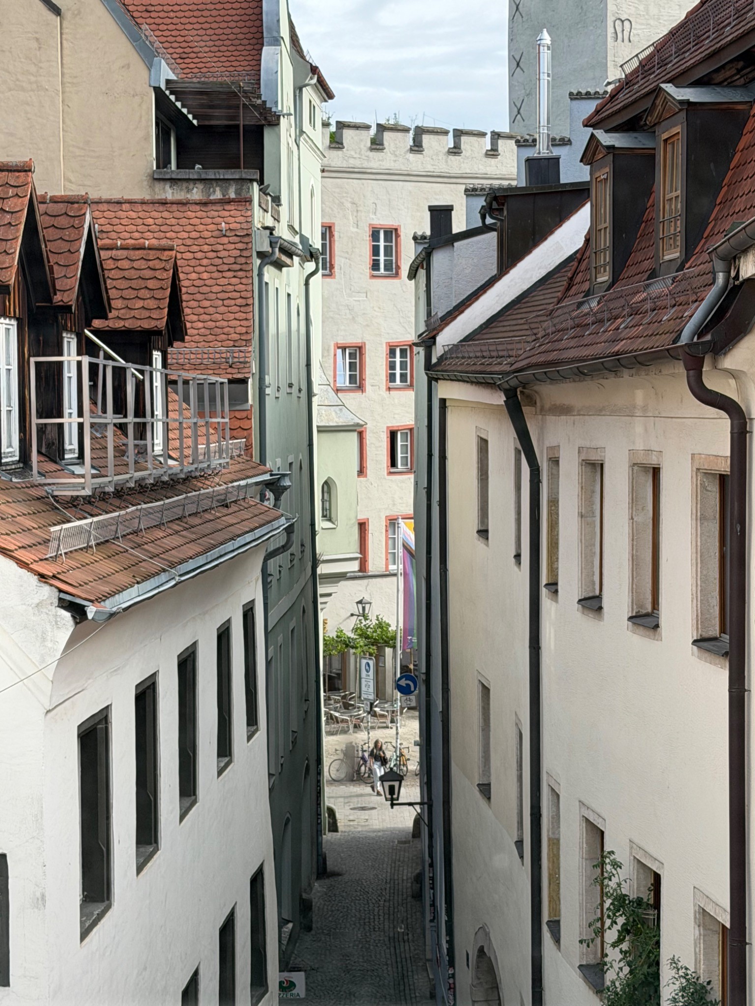 Blick zwischen historischen Fassaden und Ziegeldächern in eine schmale Regensburger Altstadtgasse.