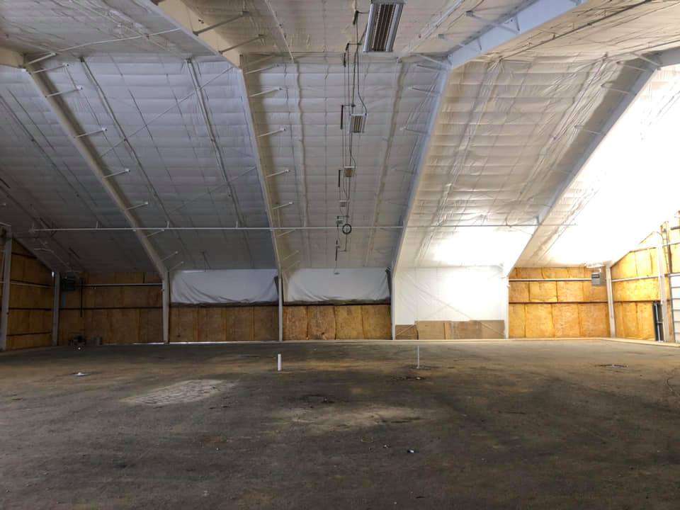 A spacious, empty interior with high ceilings and a concrete floor, featuring wooden walls and overhead lighting.