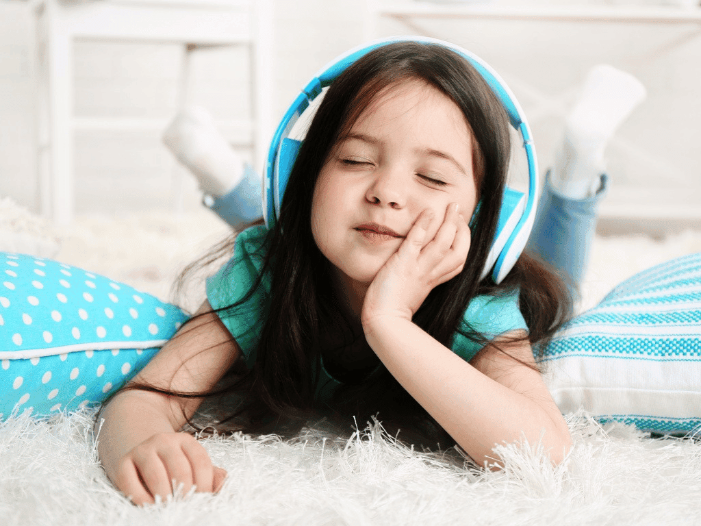 A young girl laying down wearing blue headphones lsitening to the Sound Sanctuary