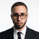 Portrait of a woman with long, smooth hair swept to the side, in a dark t-shirt, on a plain background.