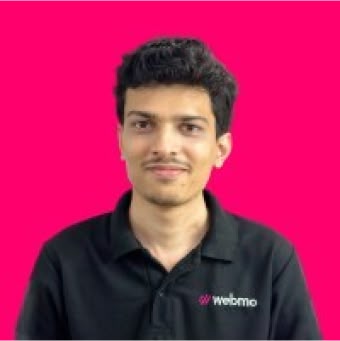 A smiling young man in a black polo shirt poses against a bright pink background.