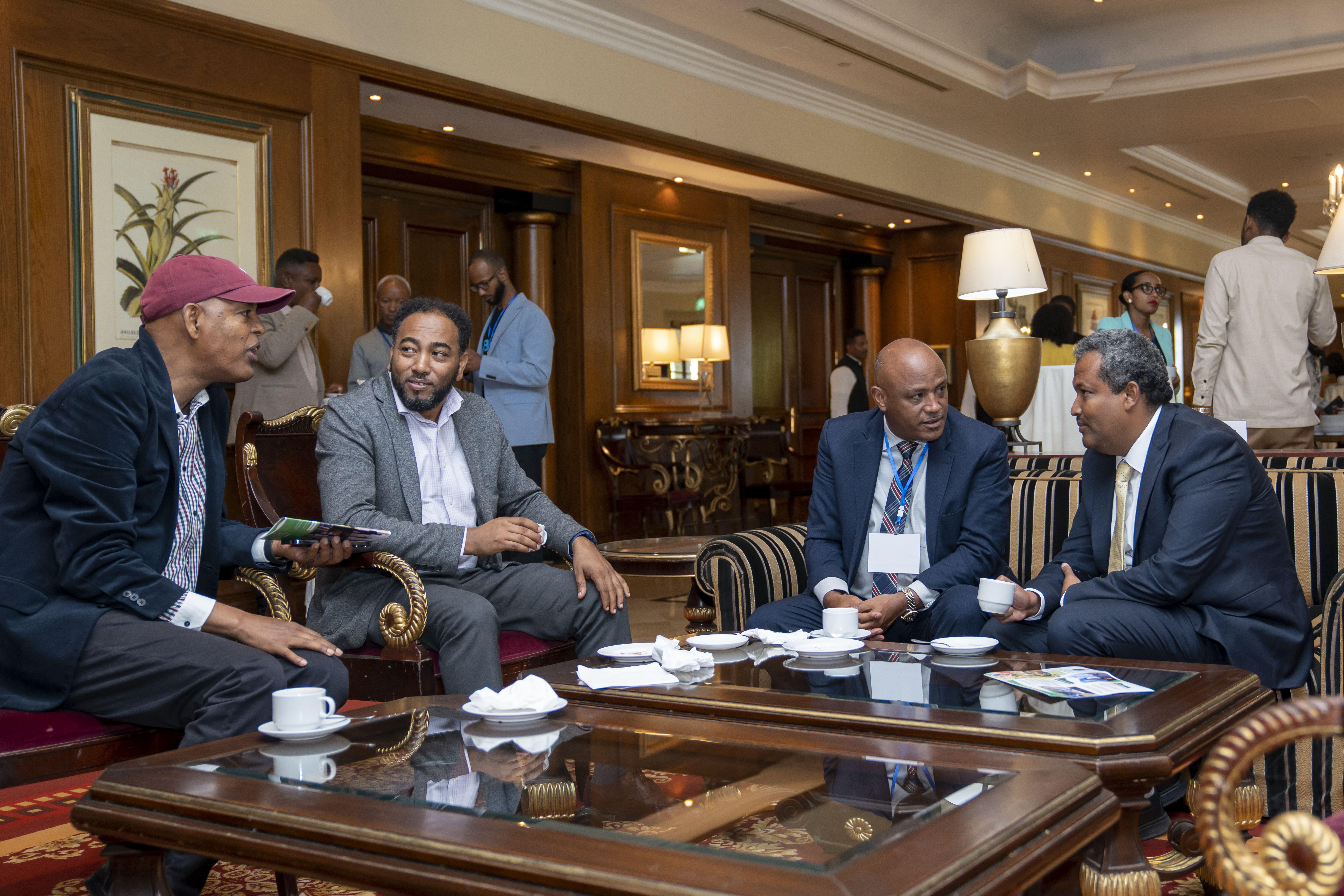 A smiling young man with crossed arms, wearing a plaid shirt and white t-shirt, poses against a dark background.