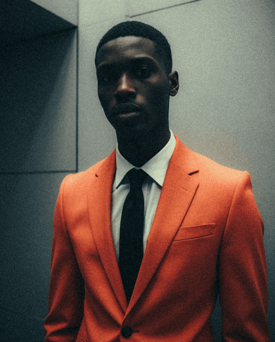 Male model in a orange suitstanding in a concreate room