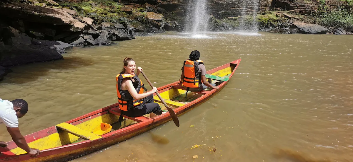 Travelers paddle a traditional canoe toward a waterfall.