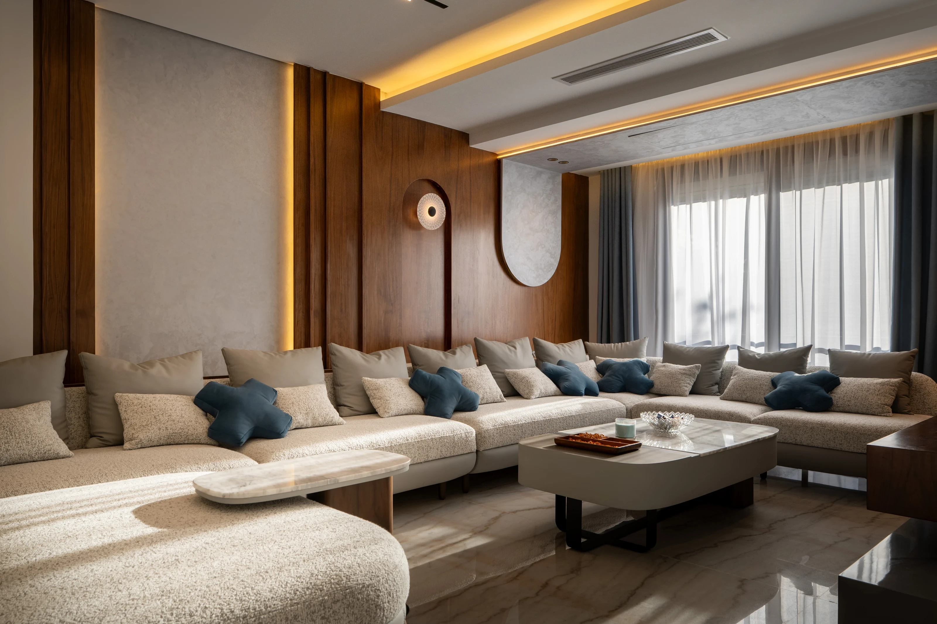 Wide view of the Mivida Twin Villa living room with custom seating, walnut wall panels, and layered lighting.