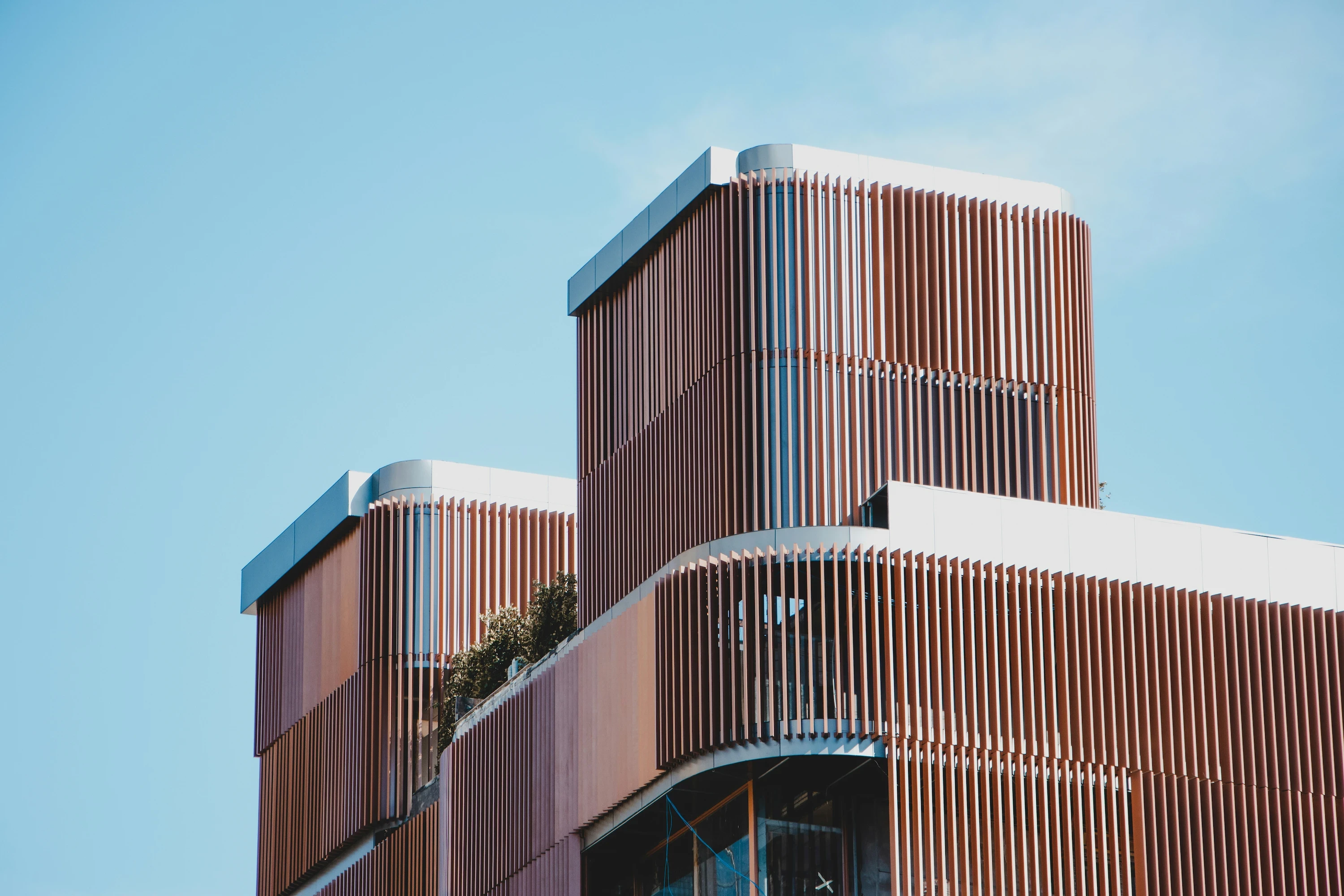 Modern, multi-tiered building blocks featuring warm brown vertical wooden cladding and louvers against a bright blue sky.