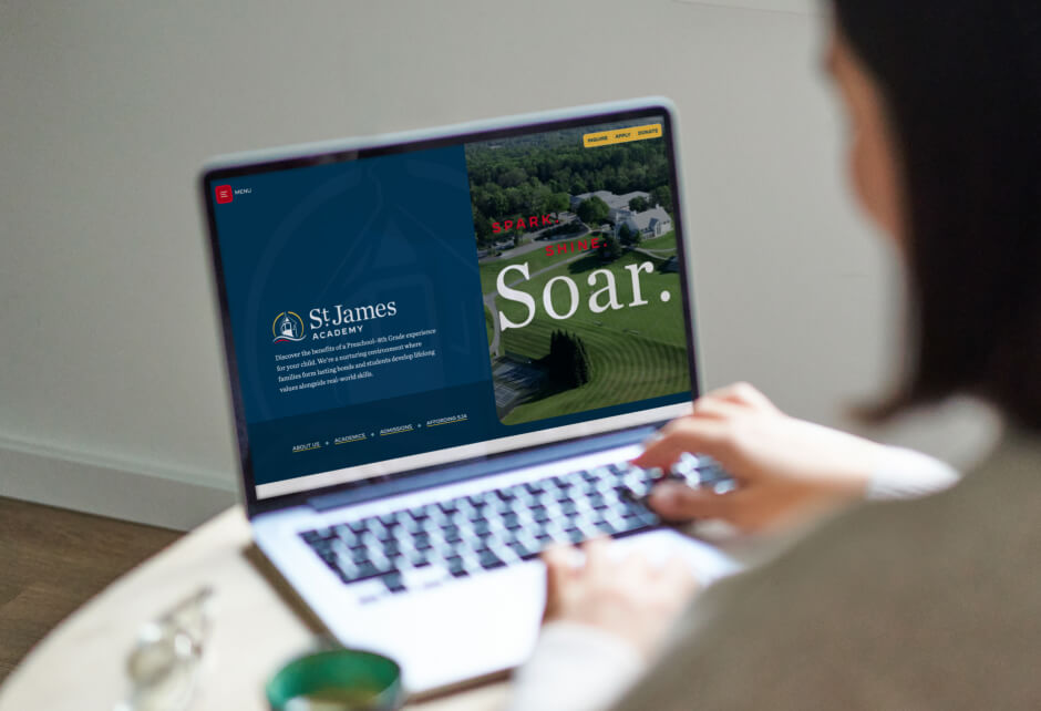 Person using a laptop with the St. James Academy website open, showcasing the school’s logo, name, and an aerial campus view with Soar—all capturing the authenticity and brand truth at the heart of St. James Academy.