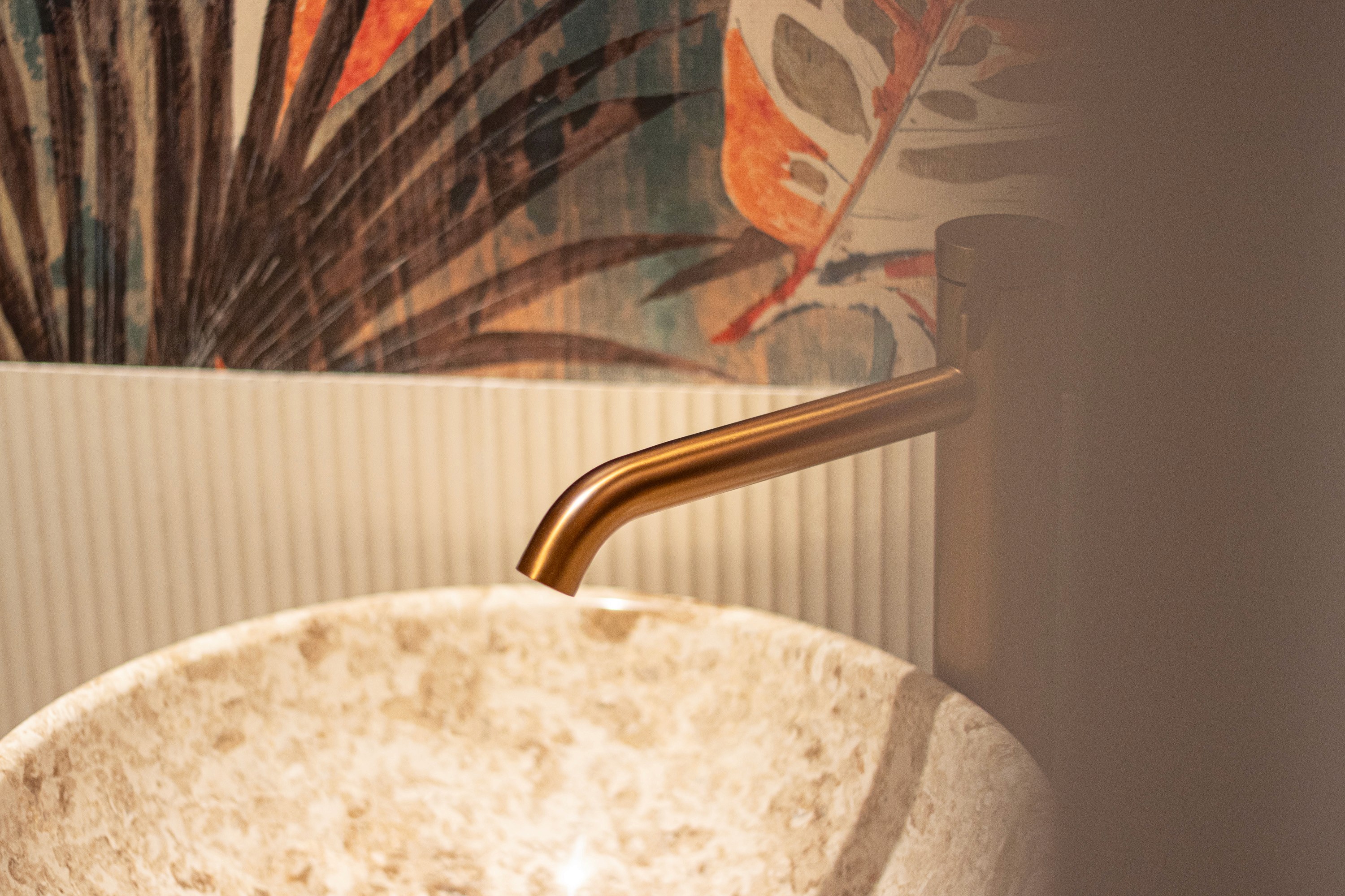 A brass tap arcing over a stone basin, against banana leaf wallpaper