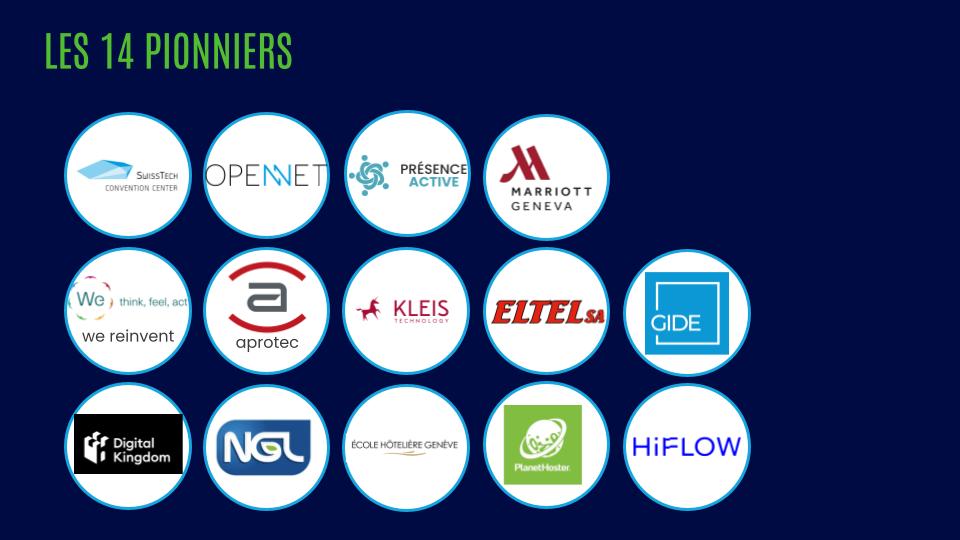 A young person with curly hair smiles at the camera while sitting in front of a laptop against a dark background.