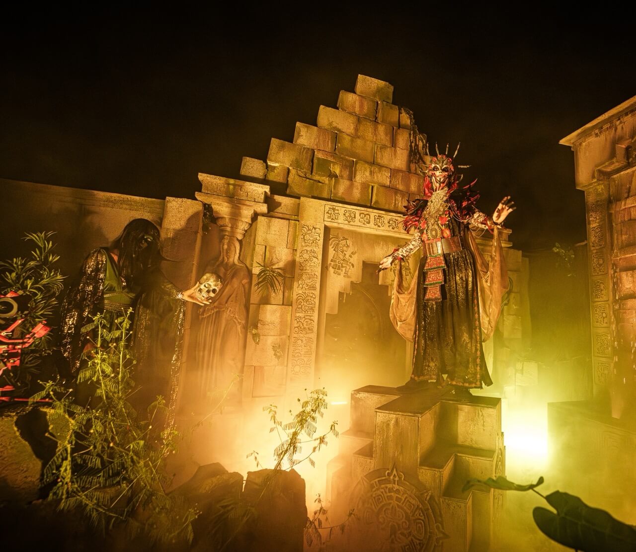 Masked scare actors outside a ruined temple set filled with yellow fog