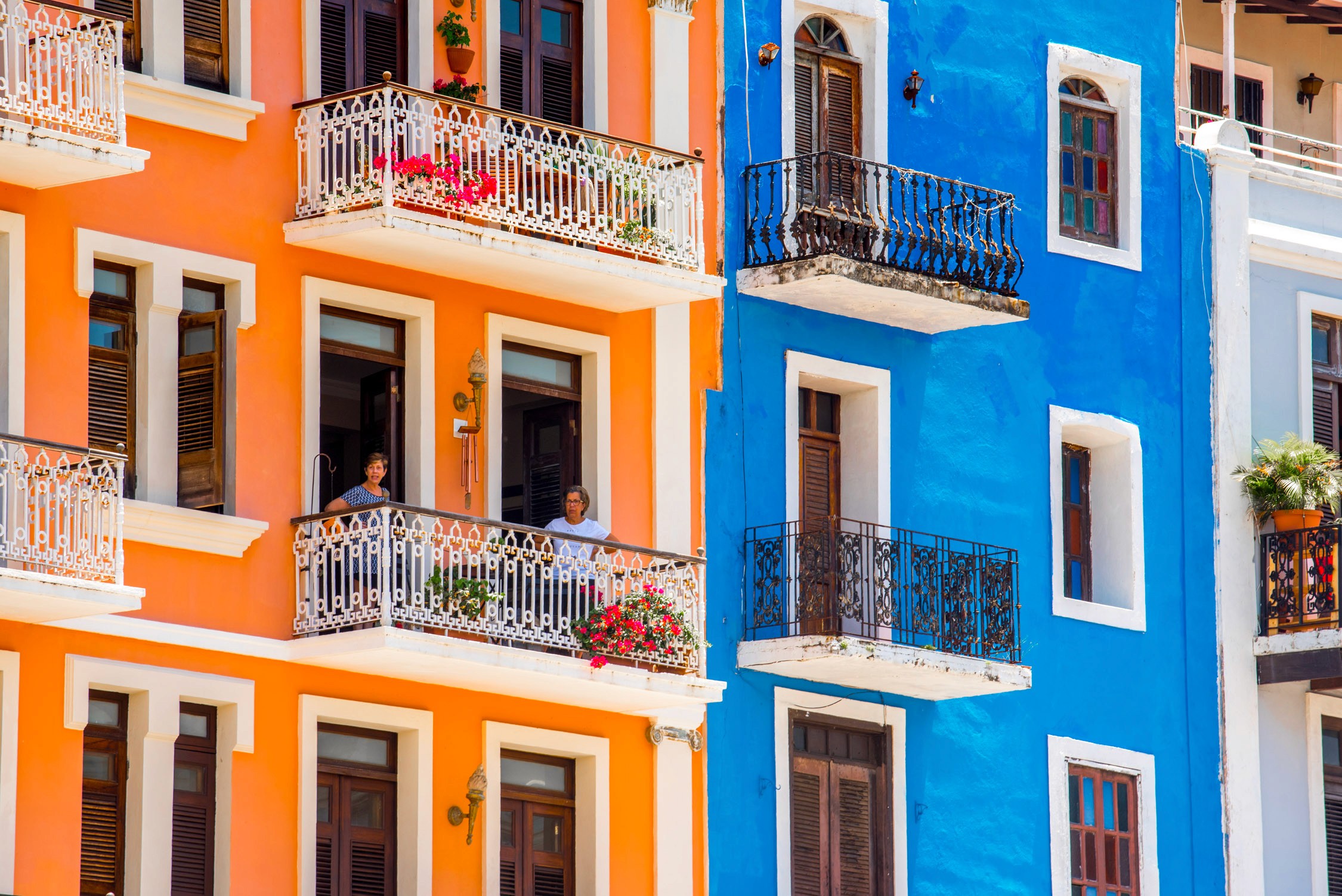 Vibrant facades of buildings in warm orange, bright blue, and white showcase colorful architectural details under clear daylight.