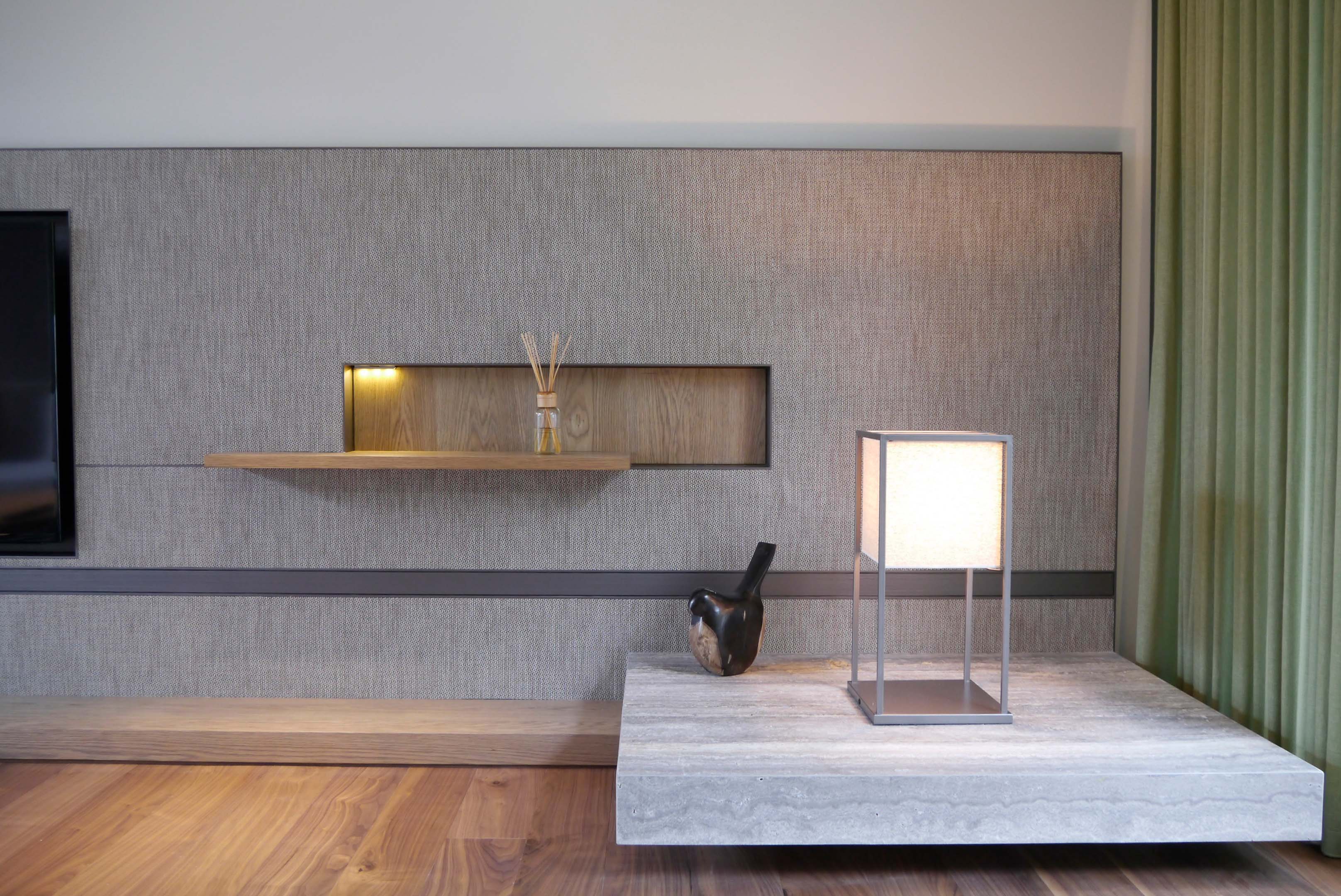 灰色紋理牆面與嵌入式木層架搭配擴香瓶與陶瓷鳥雕飾，右側為石材燈座與綠色窗簾構成細節景觀