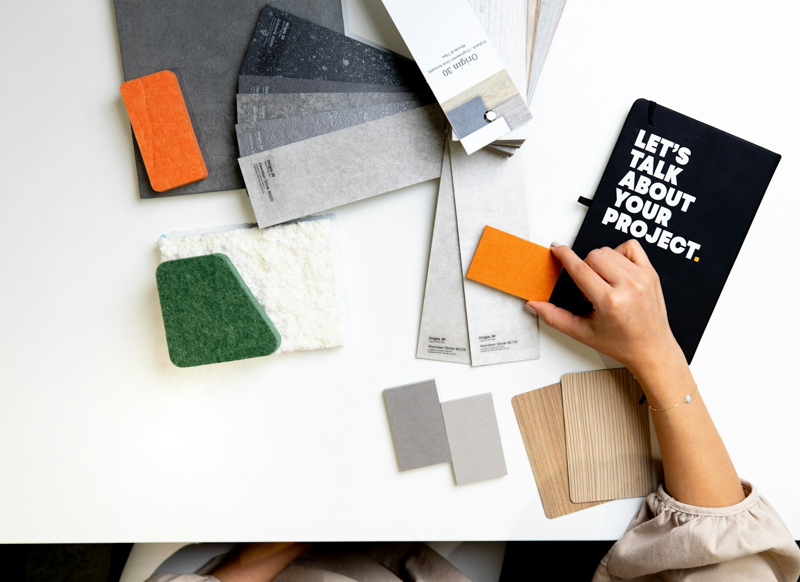 A person holding an orange material sample over a white desk with design swatches