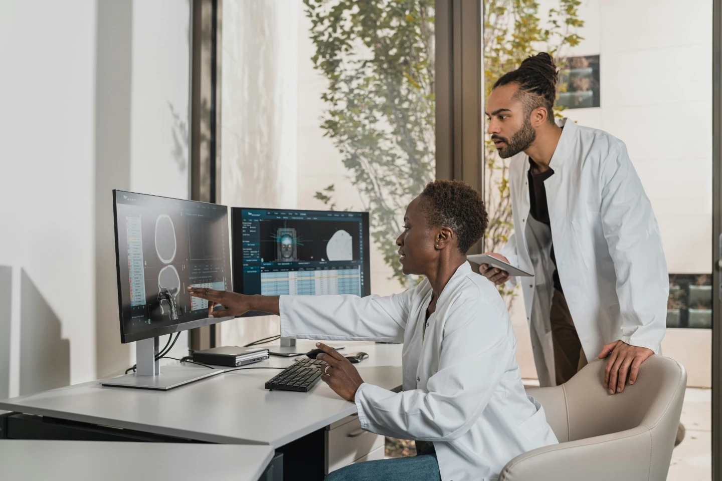 Female doctor pointing at monitor while male colleague looks over shoulder.