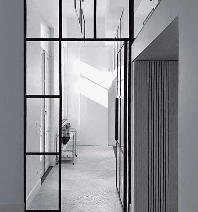 A modern, minimalist hallway featuring glass partitions, light streaming in, and clean architectural lines.