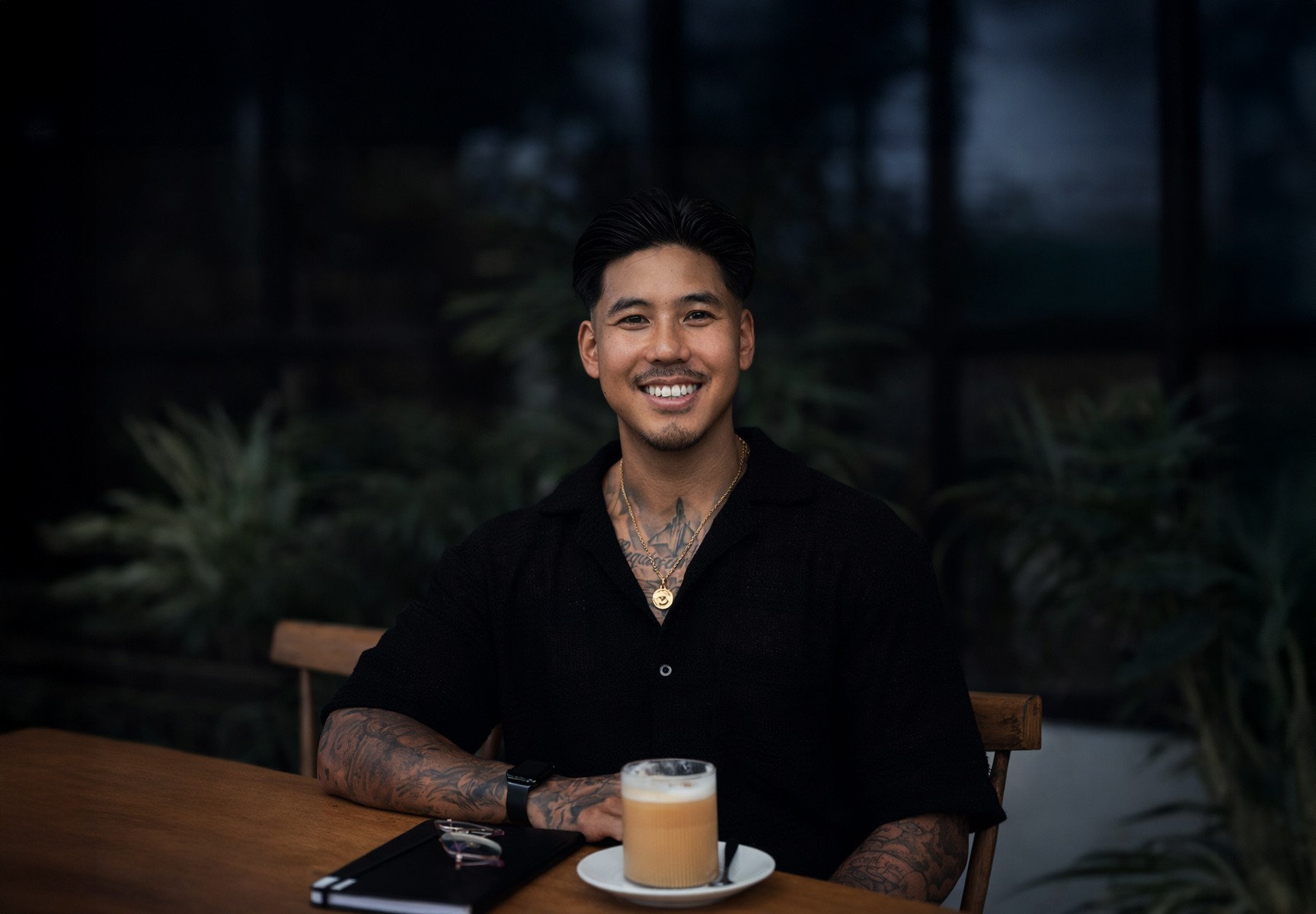 A person in an orange jacket and sunglasses, with braided hair, against orange.