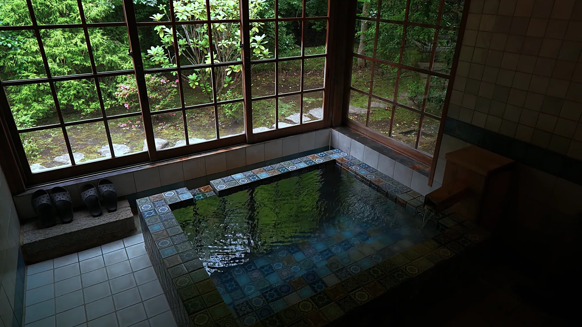 A tiled indoor bath with slippers set at the edge