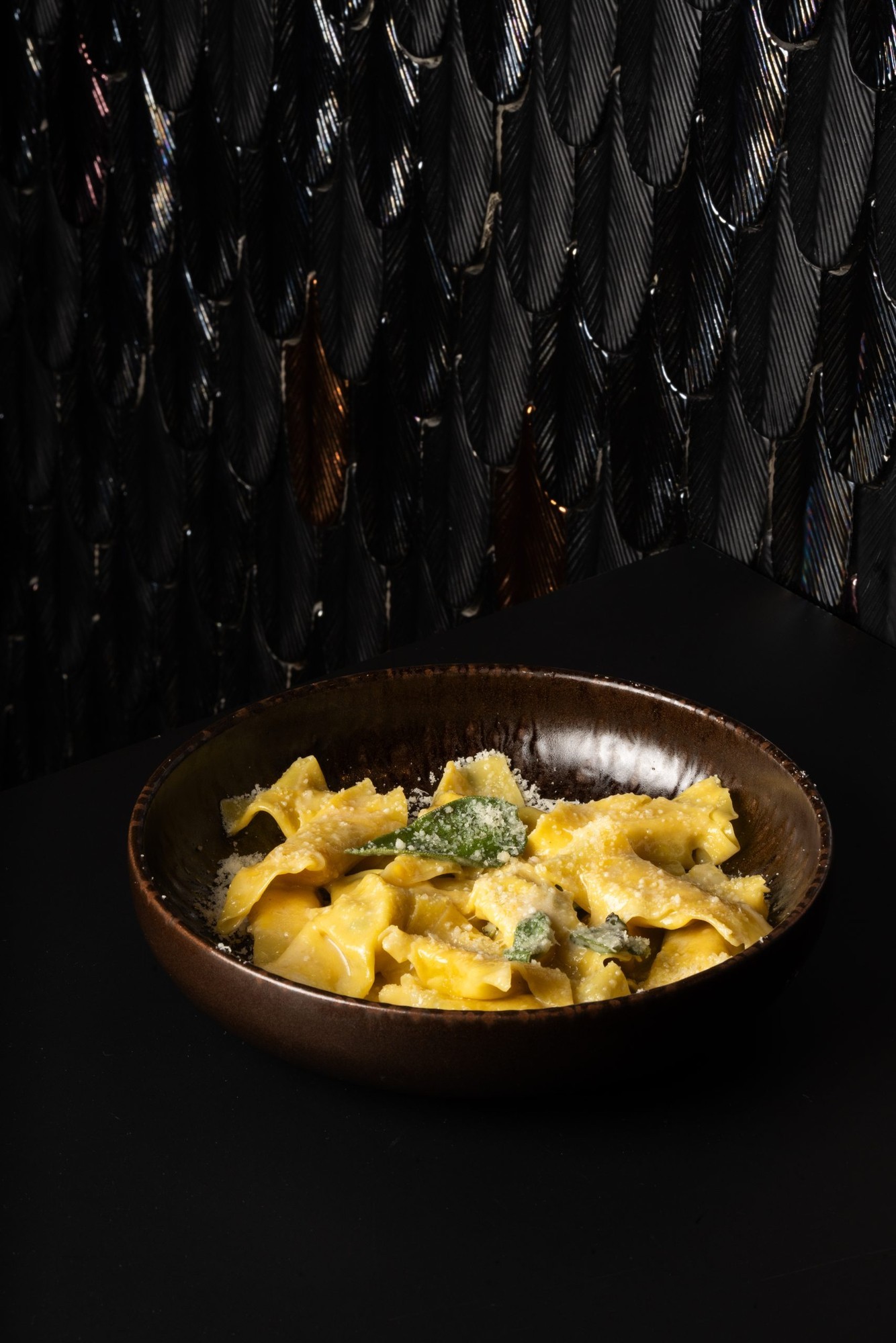 Casoncelli con foglie si salvia in superficie serviti in piatto fondo marrone su tavolo scuro