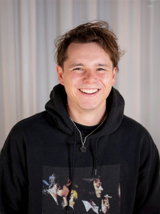 A person smiling while wearing a hooded sweatshirt.