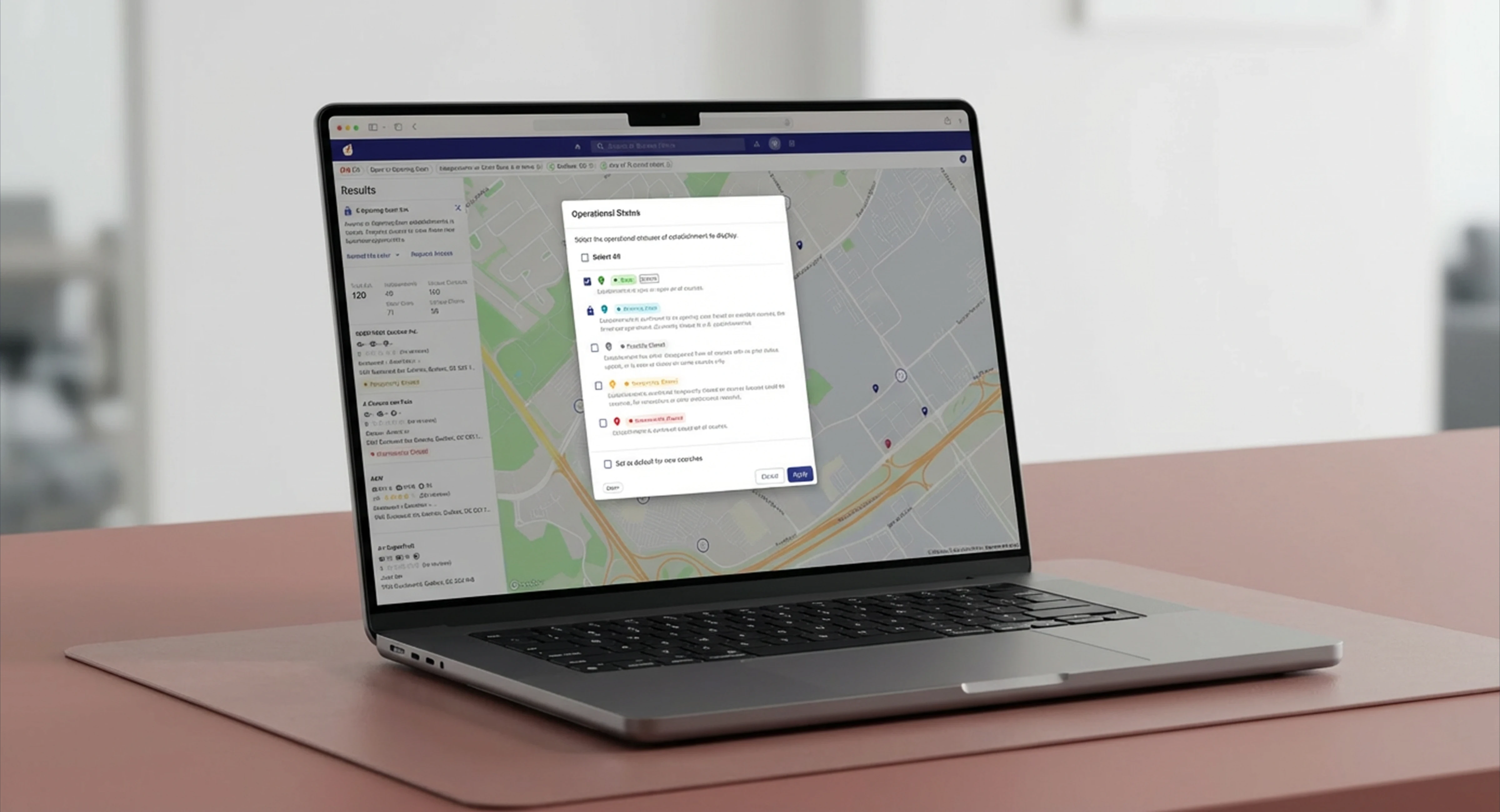Laptop on a brown desk displaying a map-based web application with an open dialog for selecting business operational status filters.