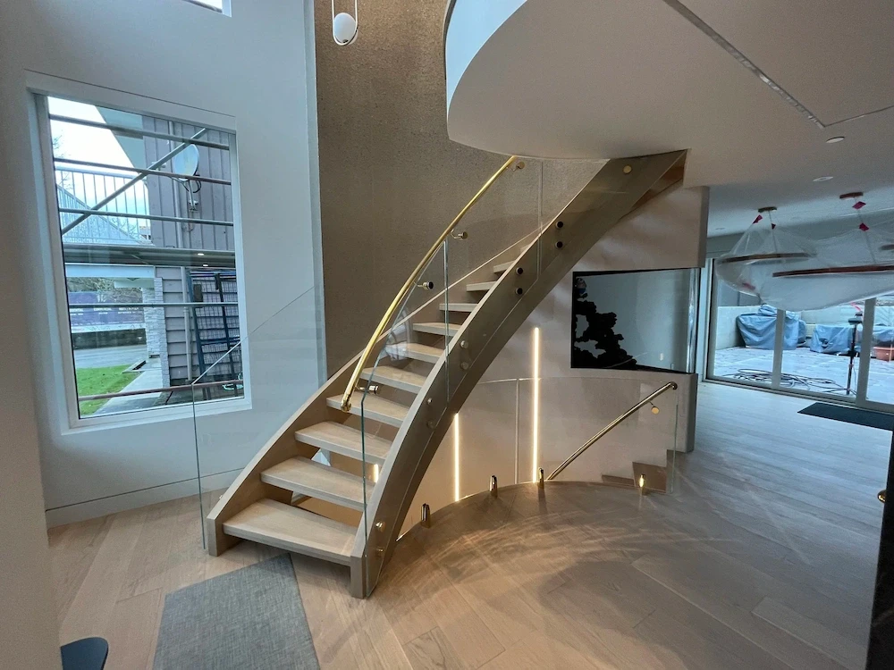 Curved glass railing on a staircase with a gold handrail.