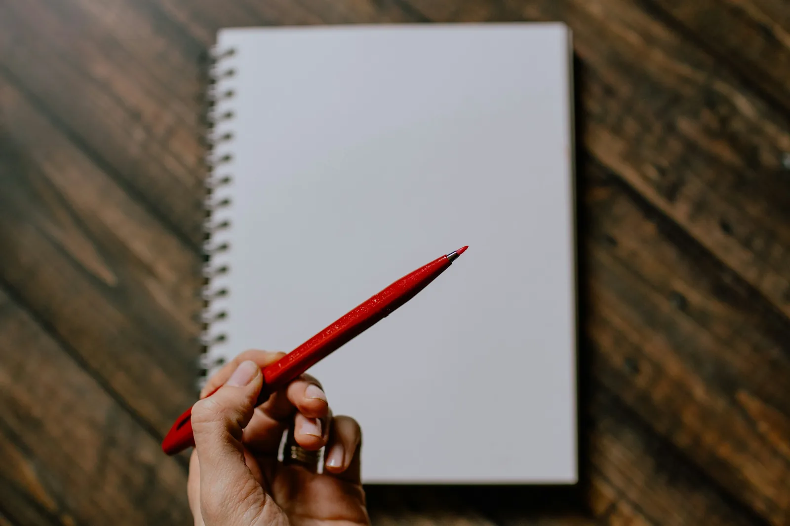 A hand holding a red pen over a blank spiral notebook