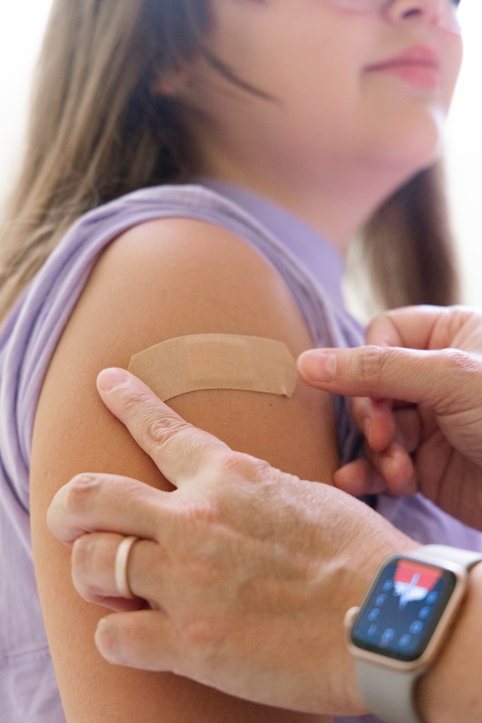 Doctor placing vaccine bandage on child's shoulder.