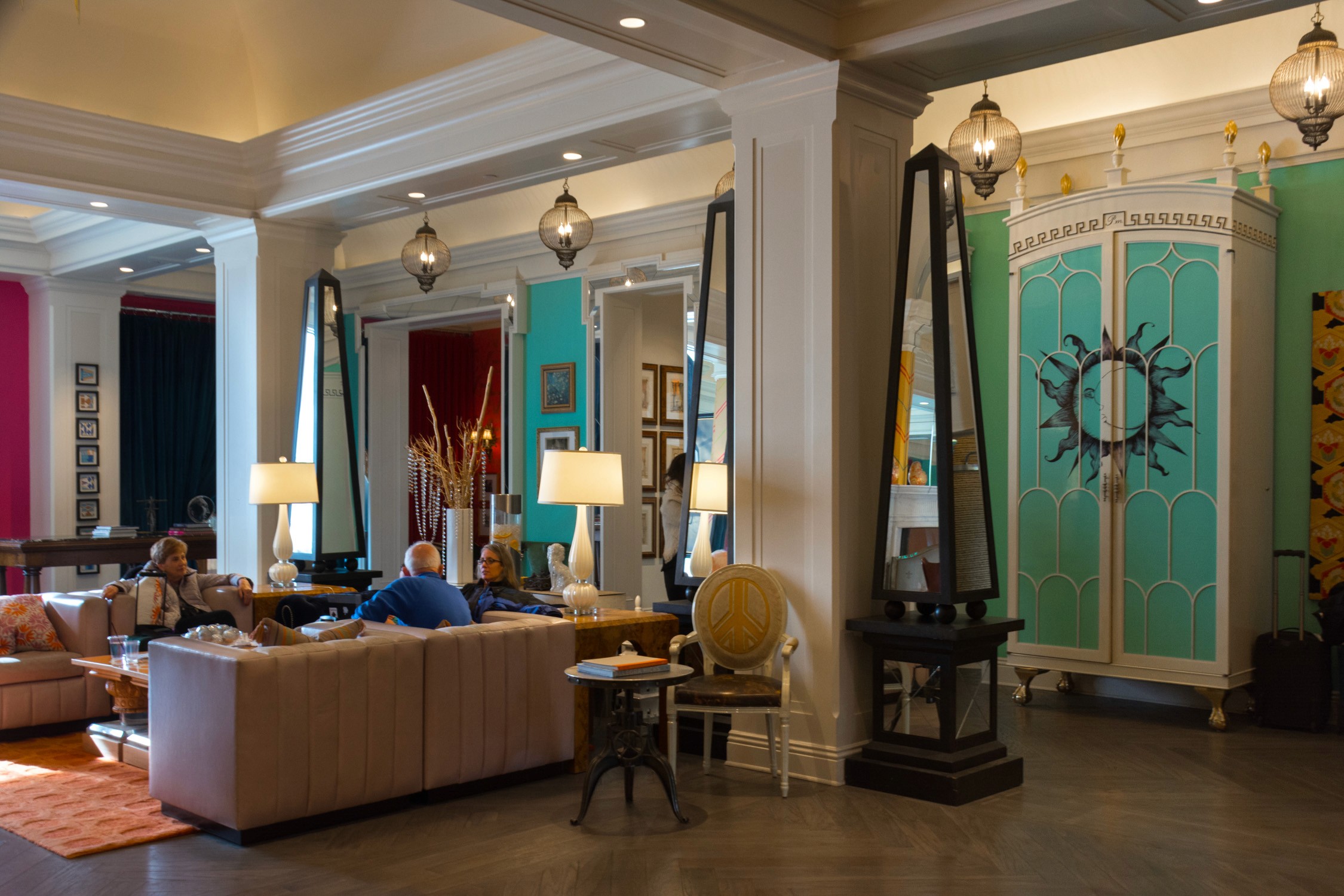 A modern hotel lobby with plush seating, a large teal and gold decorative door, and several guests relaxing in a lounge.