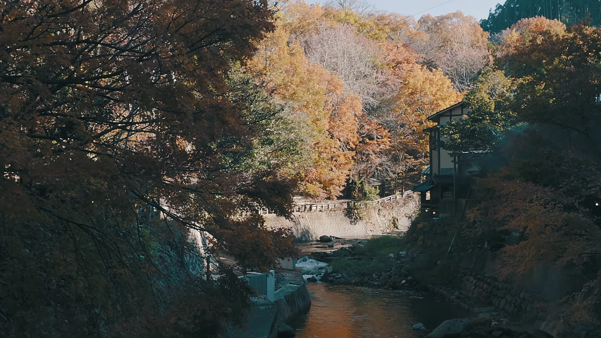 The river gorge at Kurokawa Onsen in full autumn colour, inns standing above it