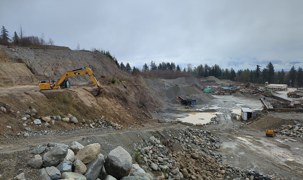 Excavator working pit slopes at Woodbrook Aggregates with processing equipment and stockpiles