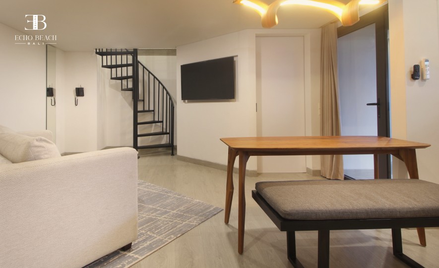 Living area of the Mezzanine apartment suite at Echo Beach, Canggu, Bali, showing the spiral staircase, dining table, and modern seating.