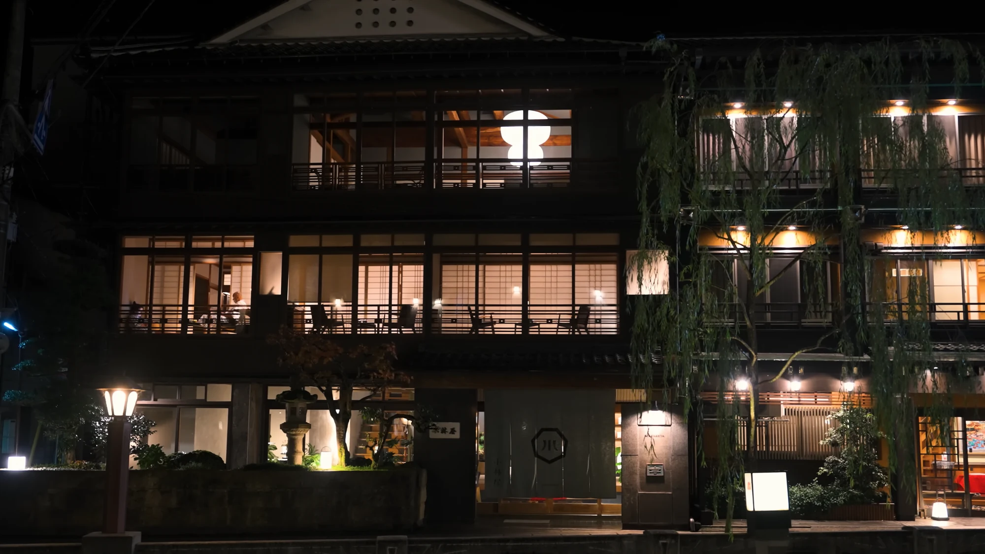 Timber inn frontages along the Kinosaki canal at night with upper windows lit.