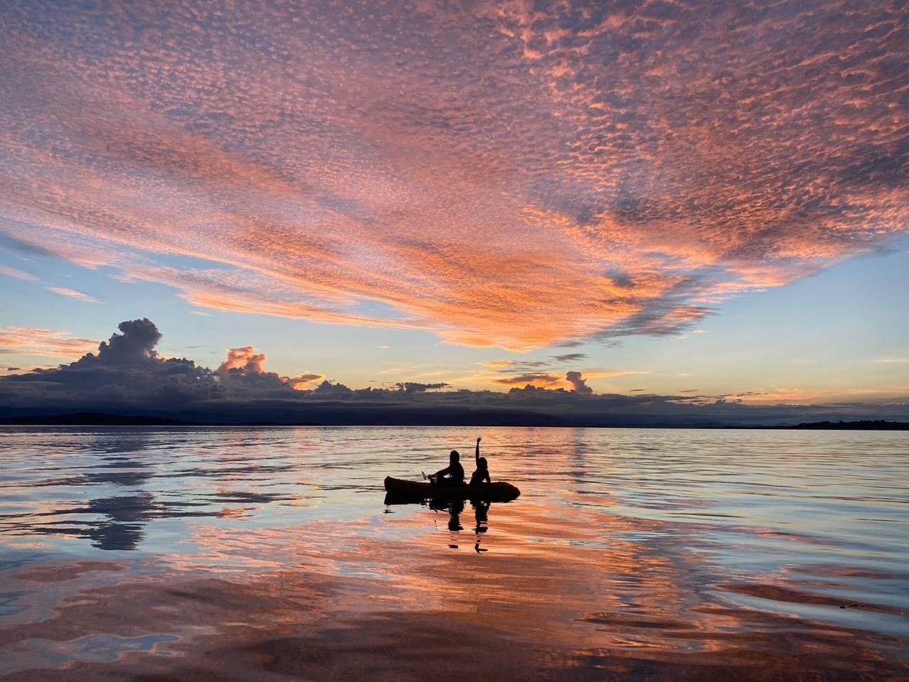 Two people silhouetted in a kayak on calm water beneath a colorful sunset.