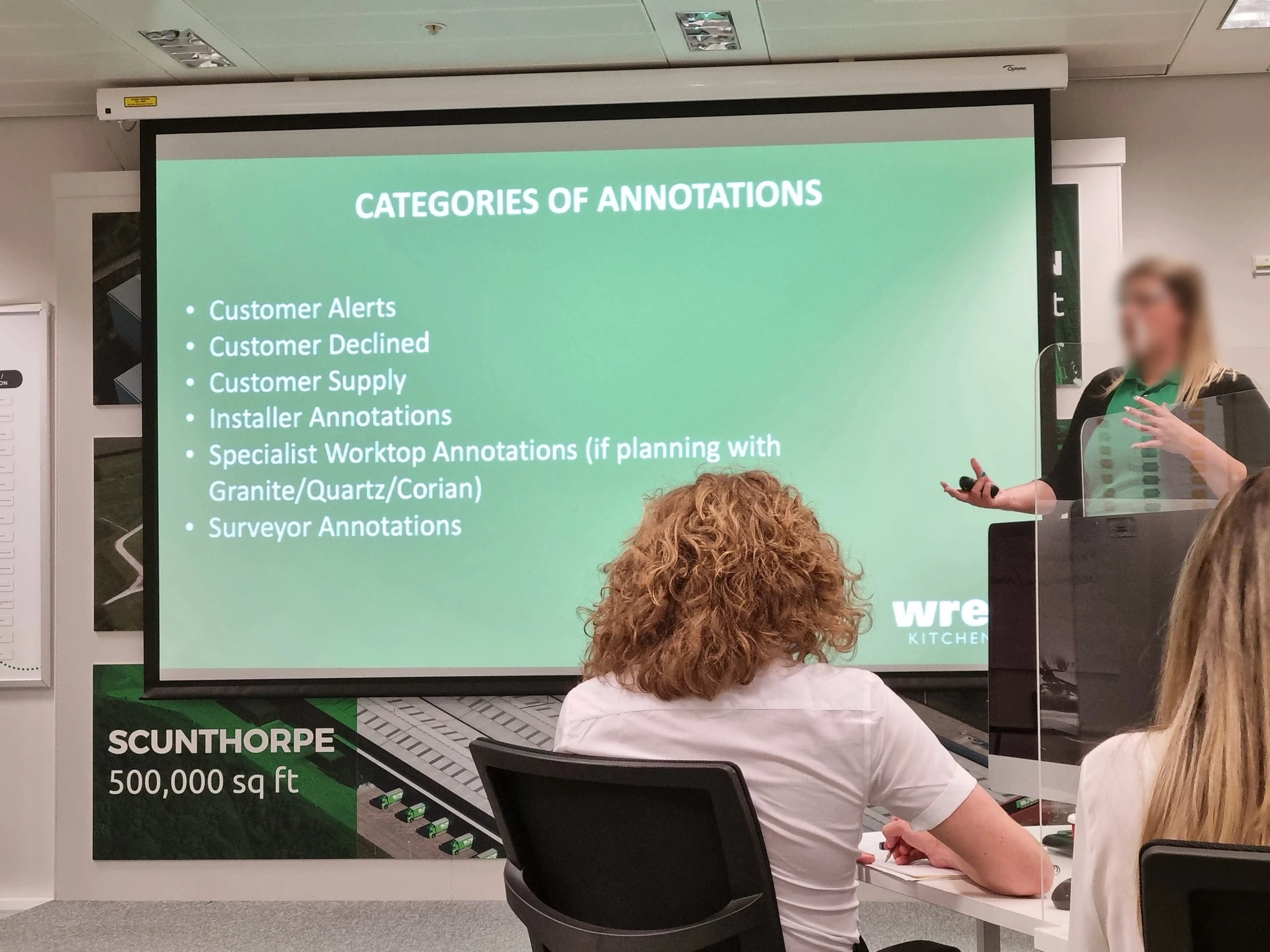 Training session for kitchen sales designers, with a presenter explaining key responsibilities on a projected slide to attendees.
