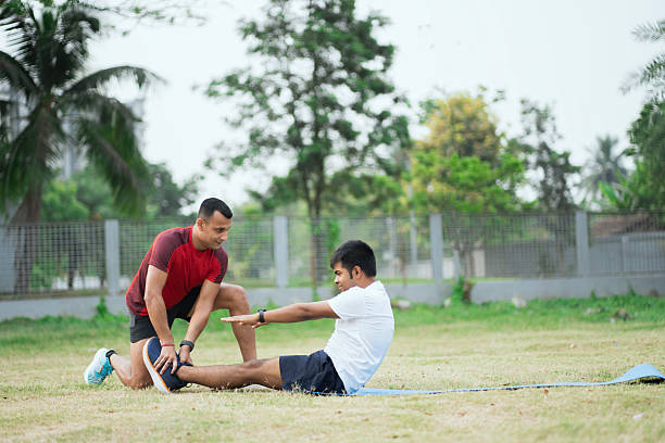 Physical trainer assisting a man with outdoor core-strengthening sit-up exercises.