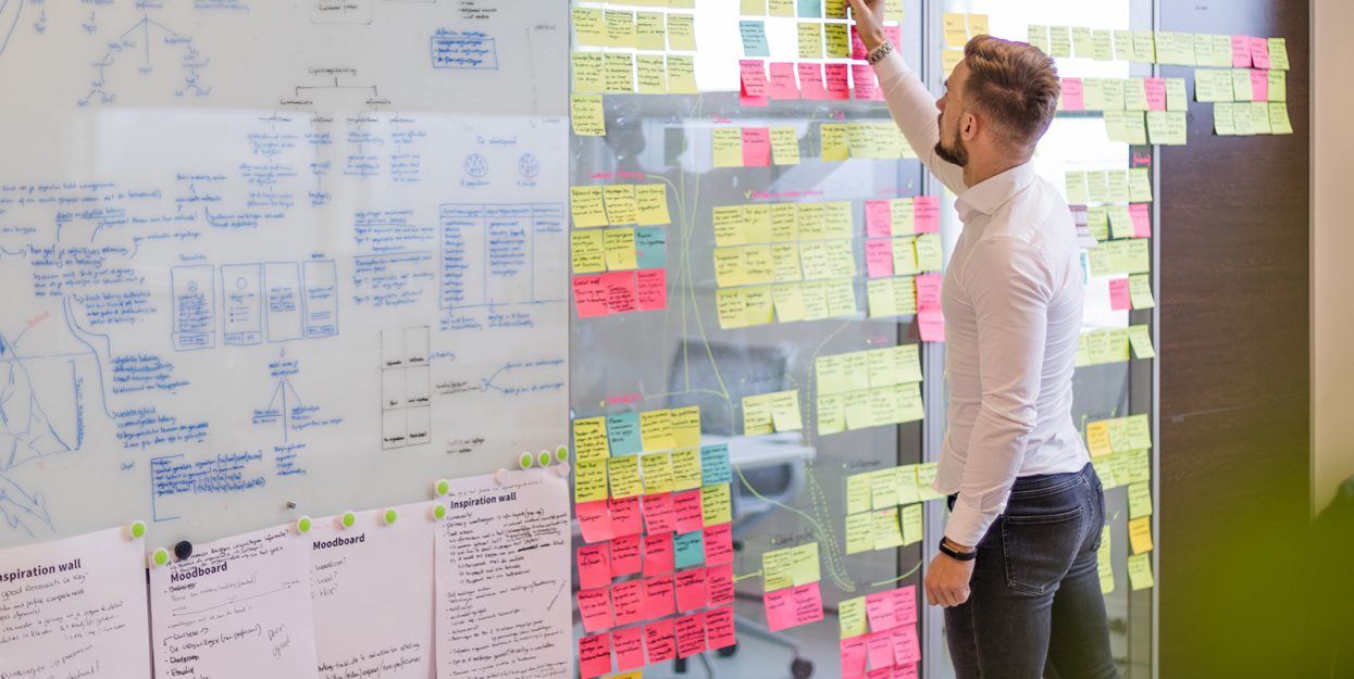 Black and white image of people working at a table with laptops, showing hands gesturing during discussion of digital content displayed on screens, with fabrica® logo in the corner.