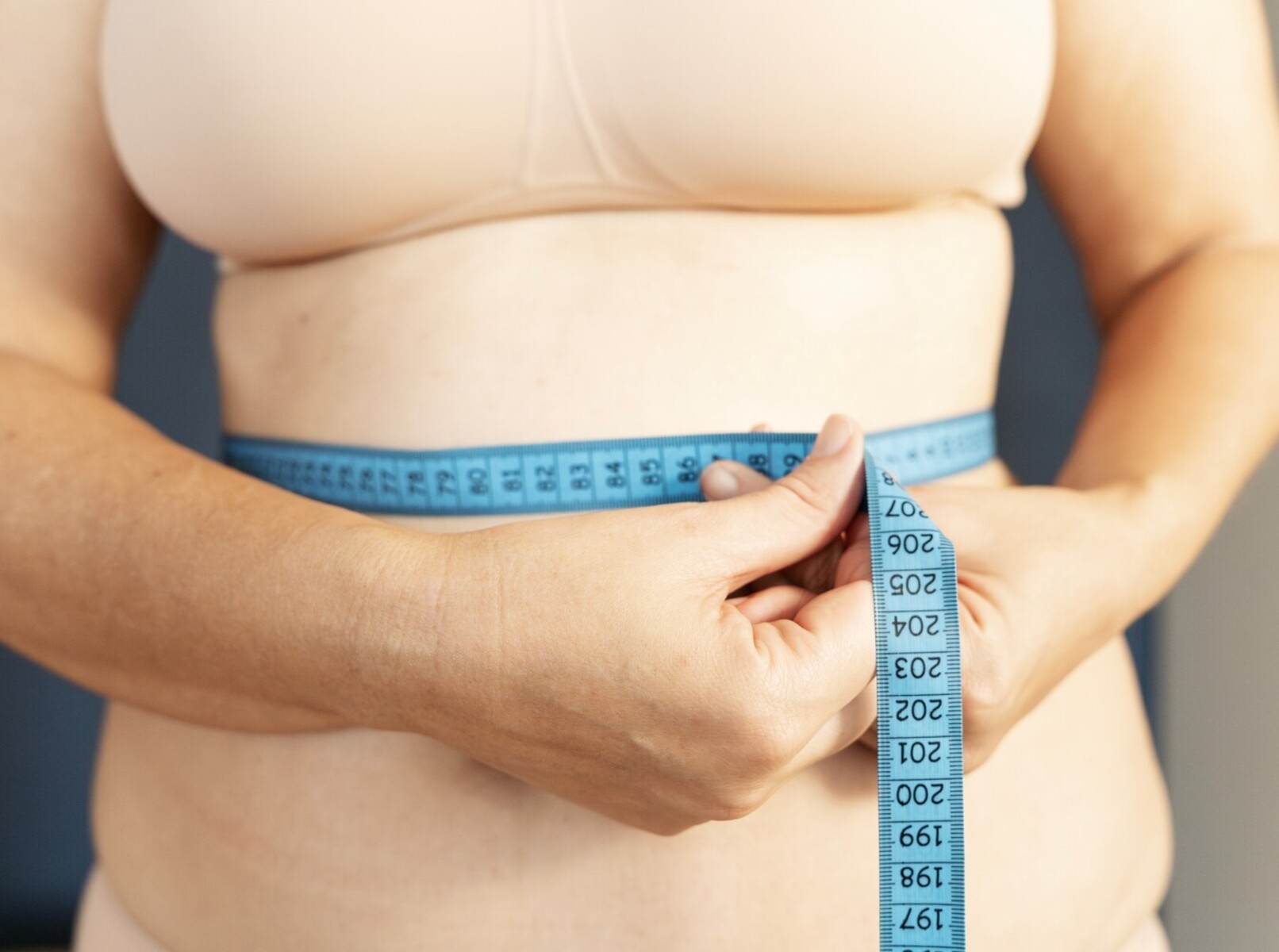 woman checking her weight loss results using a measuring tape after learning how long to ride a stationary bike to lose weight