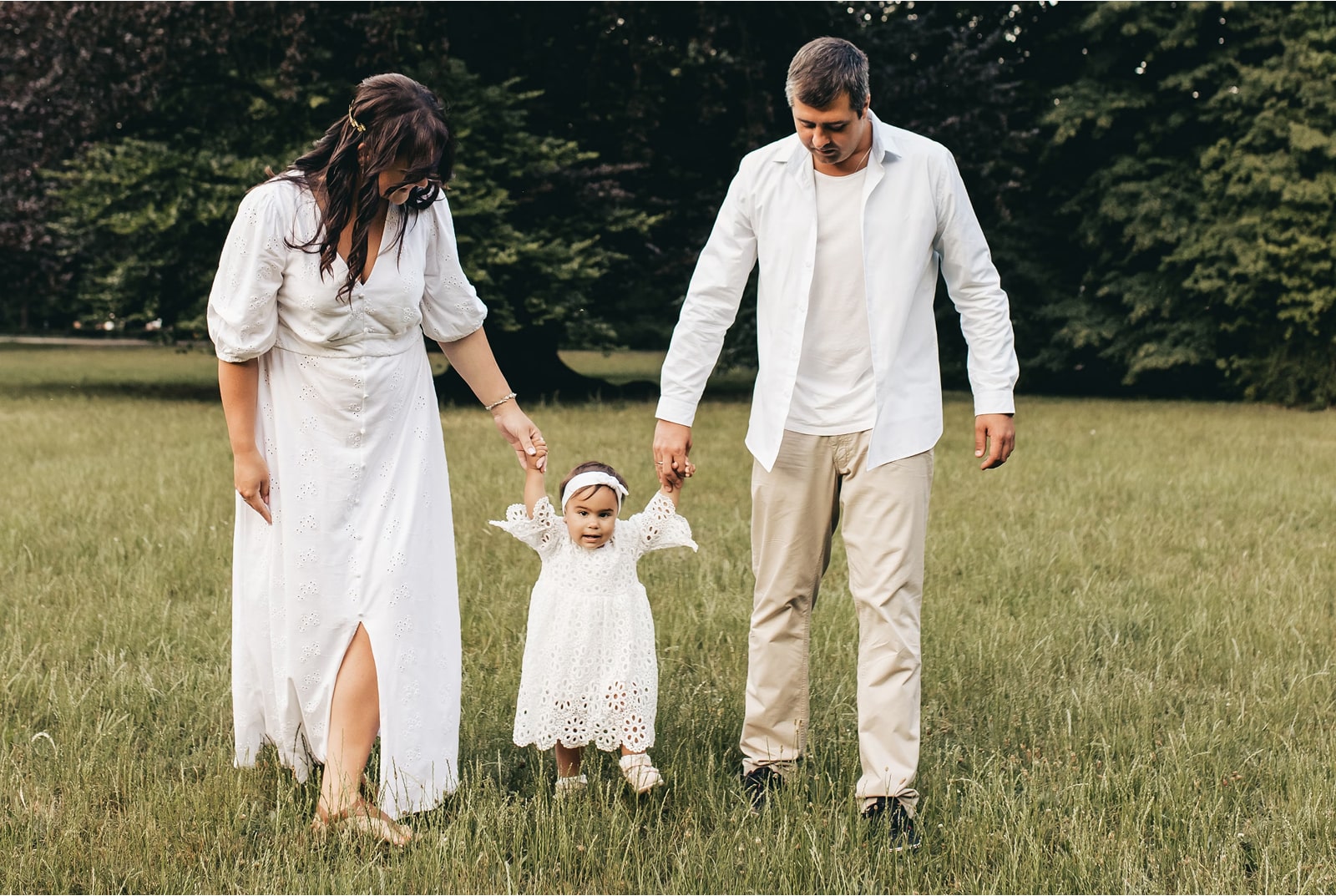 Parents walking in park holding their child's hands, representing family unity