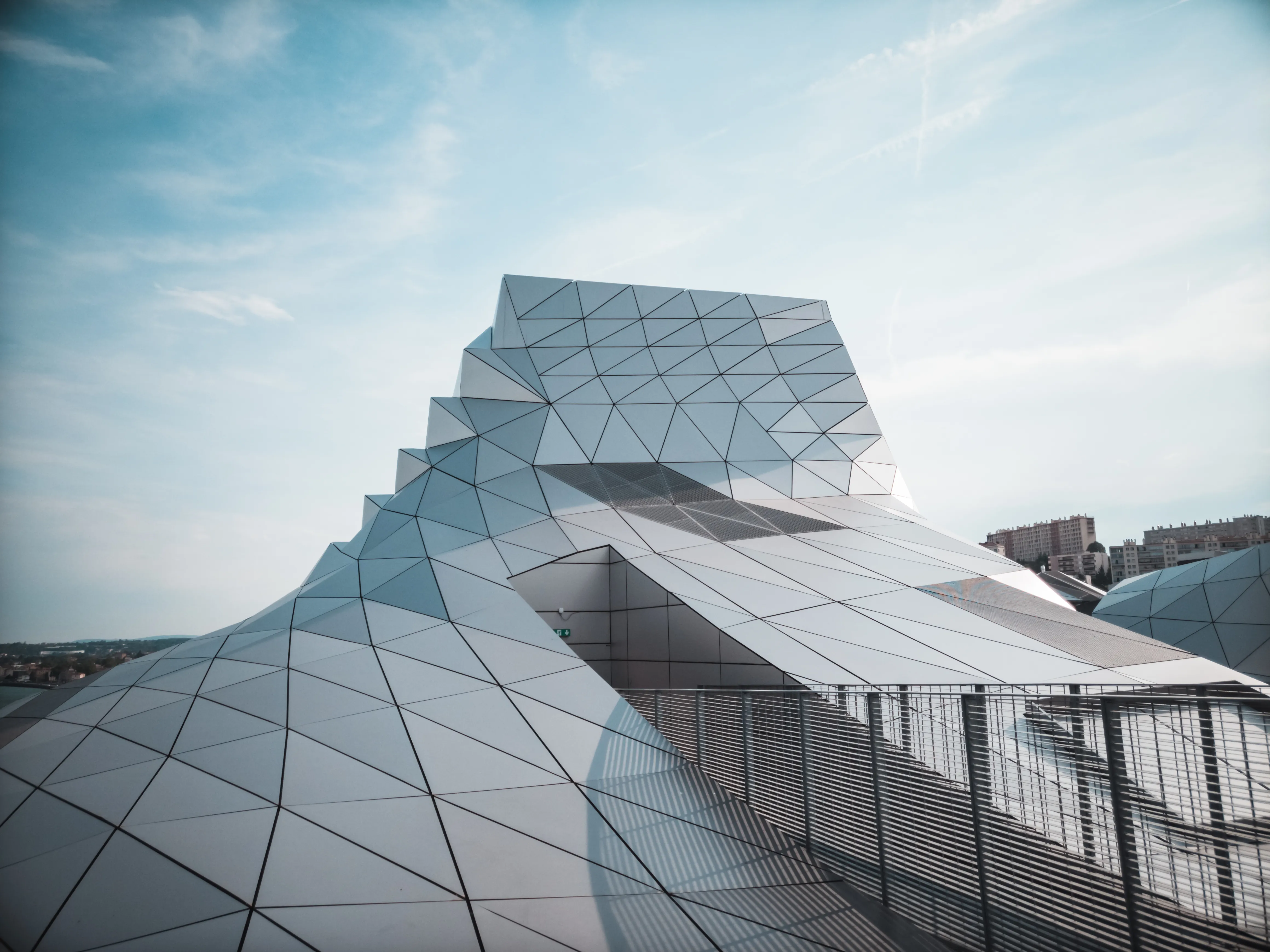 Geometric parametric architecture with a white triangular panel facade under a bright sky.