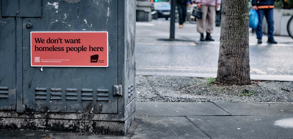 A sign that reads We Don't Want Homeless People here adhered to a cabinet in the street