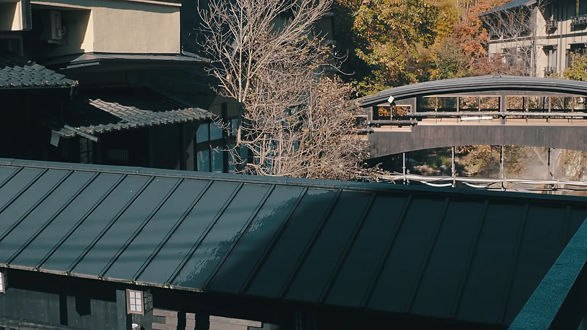 The arched bridge over the river at Kurokawa Onsen beside a metal-roofed walkway