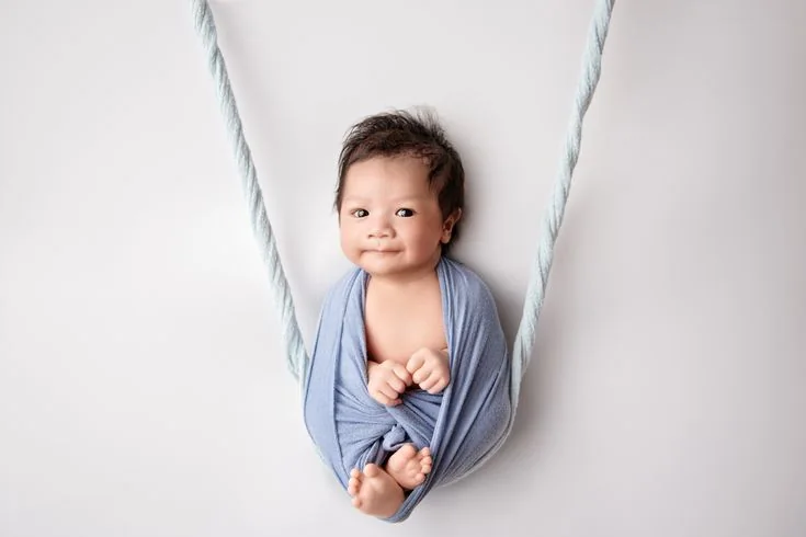 Smiling baby nestled in a blue fabric swing