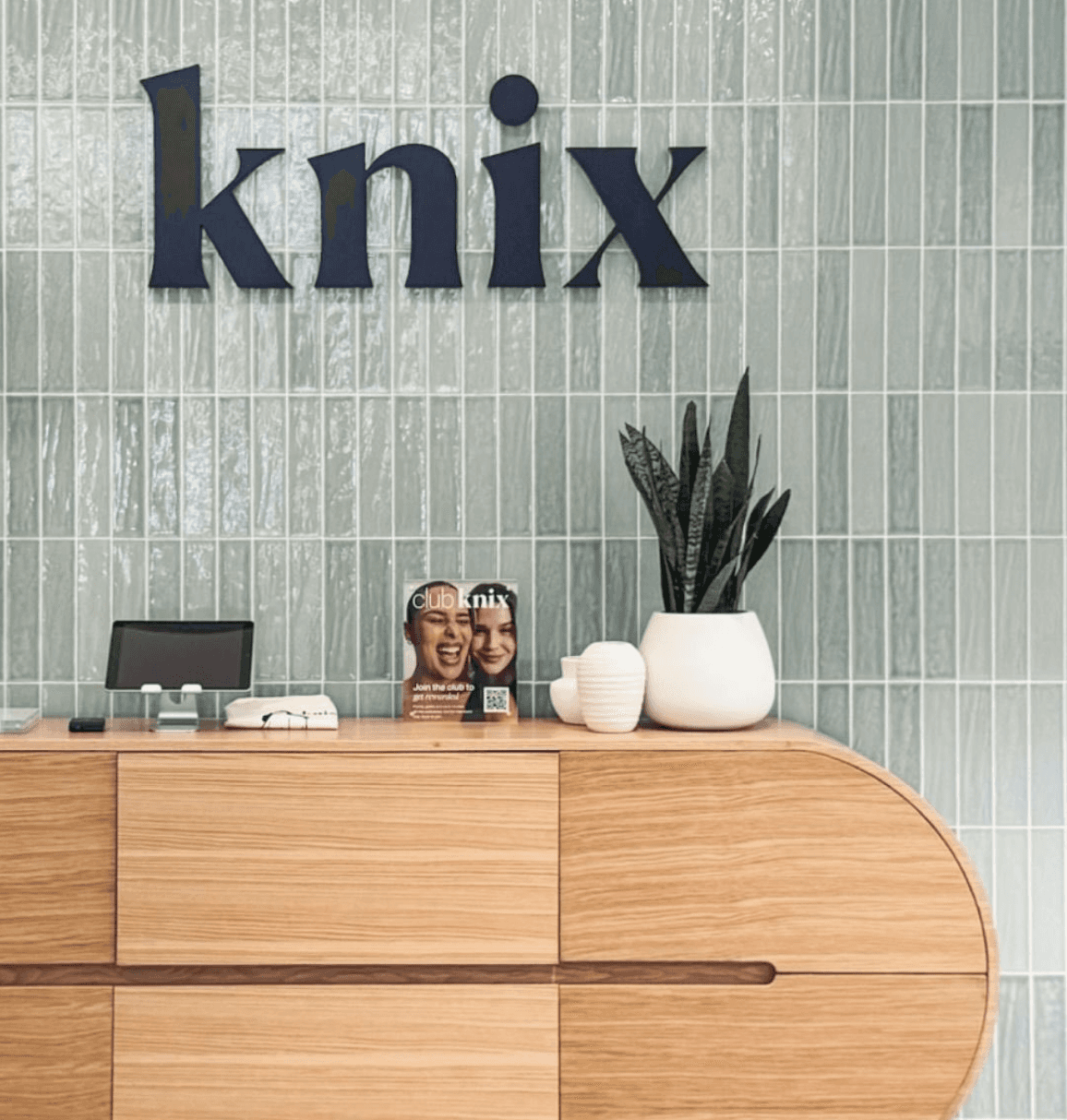 Dimensional Knix logo signage installed behind reception desk on tiled feature wall.